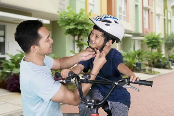Portrait of happy father fastens a helmet to his son while riding on the bicycle. Shot on the road