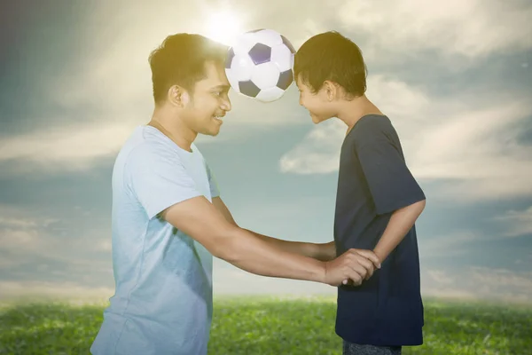 年轻人和儿子在草地上踢足球的照片 日落时拍摄 — 图库照片