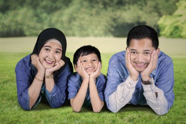 Birlikte parkta yalan sırasında kameraya bakarak mutlu Müslüman bir aile fotoğrafı 