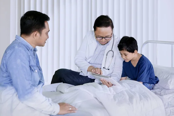 男医生在医院解释医疗报告时 在他的小病人身上展示了一个数字平板电脑的照片 — 图库照片