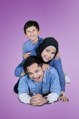 Mor arka plan ile stüdyoda yatarken oğlu ve eşi ile eğlenen genç adamın portresi