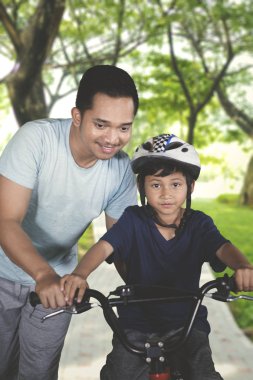 Portrait of little boy learn to ride bicycle with his father at the park. Shot outdoors