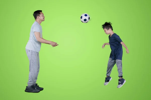 緑色の画面でスタジオでボールを見出しに彼の息子を教える若い父親の画像 — ストック写真