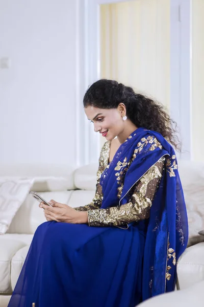 家で携帯電話を使用しながら青いサリー服を着ている美少女の画像 — ストック写真
