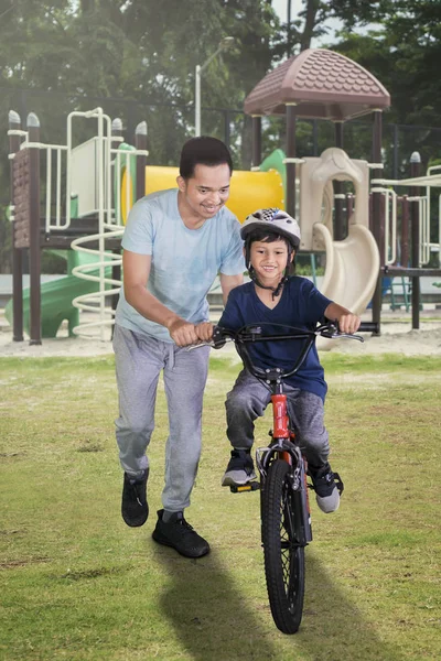 小男孩的肖像在操场上和父亲一起学习骑自行车时显得很开心 — 图库照片