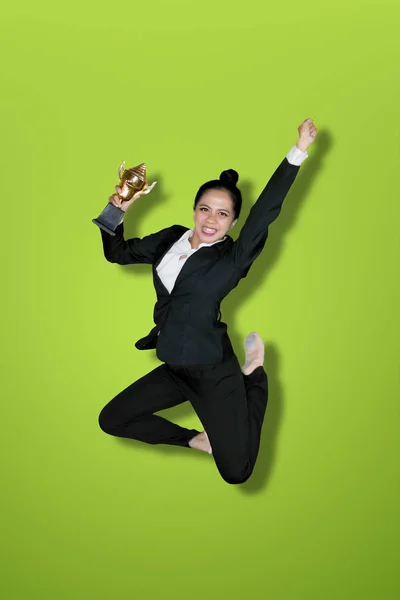 兴奋的女商人拿着奖杯 而跳在工作室与绿色屏幕的肖像 — 图库照片