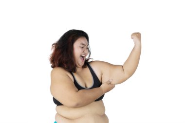 Picture of obese woman looks sad while showing her flabby bicep in the studio, isolated on white background clipart