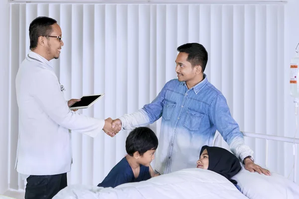 Médico Masculino Visitando Paciente Mientras Apretón Manos Con Familia Clínica —  Fotos de Stock