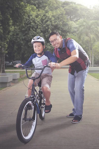 Picture of happy father guiding his son to riding a bicycle in the park. Shot at summer time