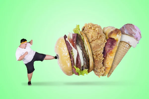 愤怒的胖子在工作室里穿着带有绿色屏幕的运动服时踢快餐的照片 — 图库照片