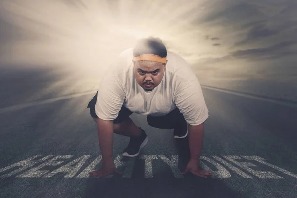 Picture of an Asian obese man ready to run while kneeling above healthy diet text on the road. Shot with sunlight background