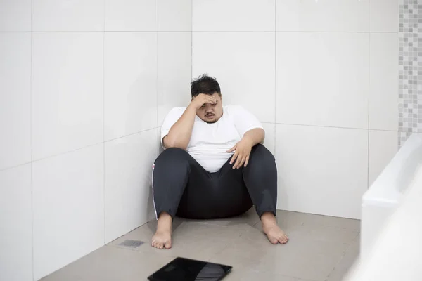 浴室のスケールで座りながら手で彼の目を覆っている欲求不満の肥満男の画像 — ストック写真