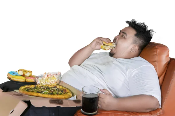不健康なライフ スタイル コンセプト 貪欲なデブ男を食べるハンバーガーやソファでは 白い背景で隔離のジャンク フード — ストック写真