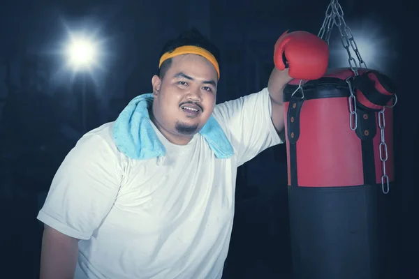 Picture of an obese man leaning on a bag boxing after boxing exercises in the dark room