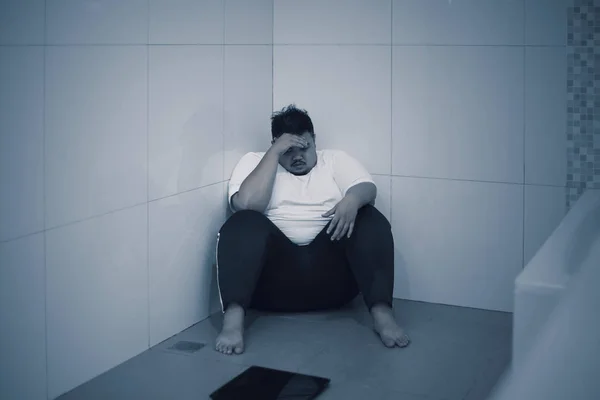 减肥失败的概念 年轻的肥胖男子坐在浴室里 拿着秤显得很难过 — 图库照片