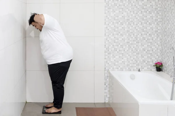 Portrait of an obese man looks shocked while standing on the scale. Shot in the bathroom