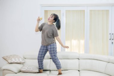 Genç bir kadın kanepede dans ederken şampanya içmek resim. Evde vurdu