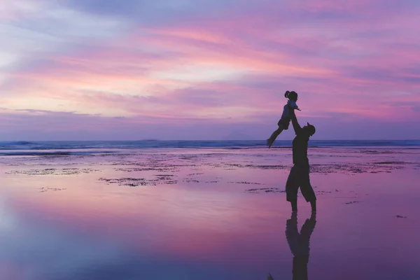 黄昏时 年轻父亲在海滩上一起玩耍时抬起女儿的剪影 — 图库照片