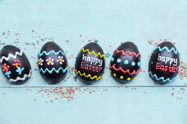 木桌上有五个装饰过的巧克力蛋的顶视图 上面有快乐的复活节文字 — 图库照片
