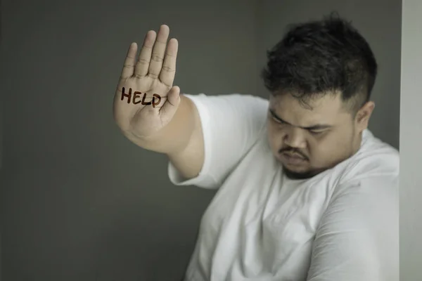 Picture of Asian obese man looks sad while showing help word on his palm in the dark room