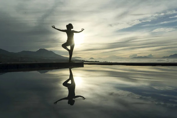 在池畔冥想时做瑜伽练习的年轻女子的剪影 日落时拍摄 — 图库照片