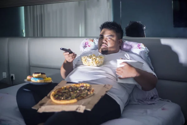 Asian fat man eating junk foods on the bed — Stock Photo, Image