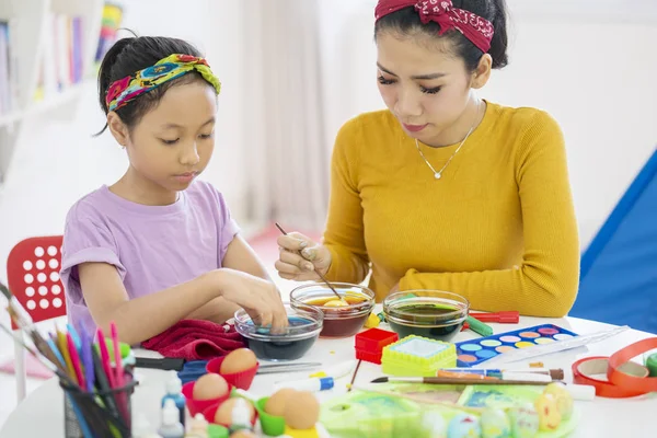 Kleines Mädchen unter Anleitung ihrer Mutter Ostereier färben — Stockfoto