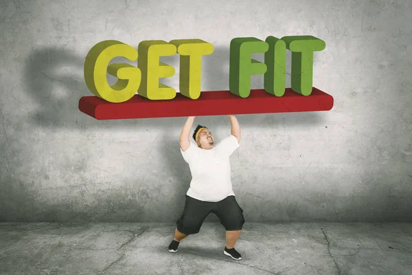 Young obese man carrying fat word on studio — Stock Photo, Image