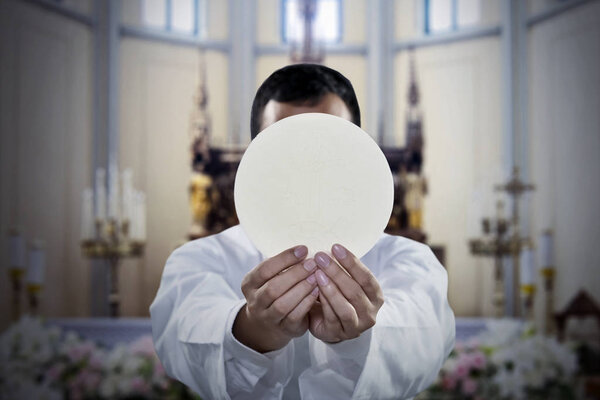 Hands of pastor holding a bright communion wafer