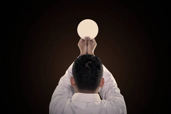 Hands of pastor holding a bright communion wafer — Stock Photo, Image