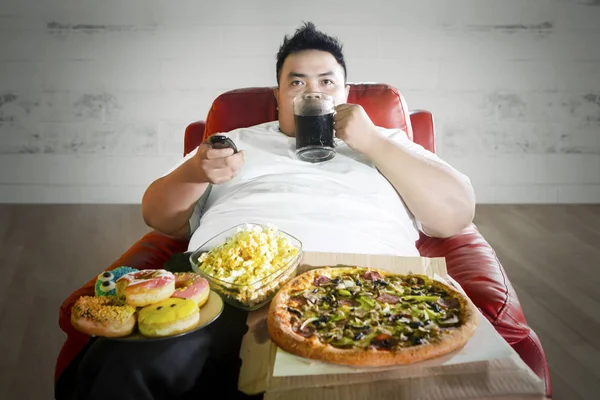 Jovem gordo desfrutando de junk foods no sofá — Fotografia de Stock