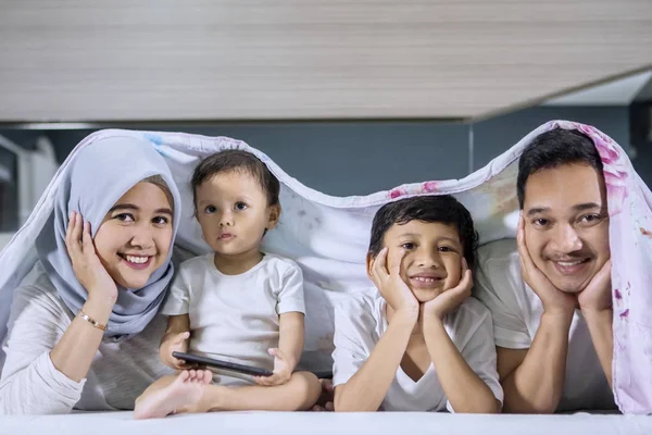 Familia feliz acostada en la cama bajo una manta —  Fotos de Stock