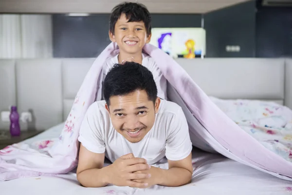 Boldog fiatalember és fia hozzábújva ágyon — Stock Fotó