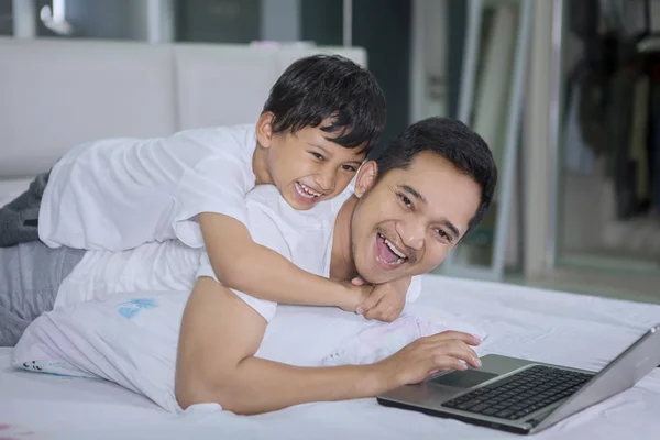 Мужчина и сын смеются во время использования ноутбука на кровати — стоковое фото
