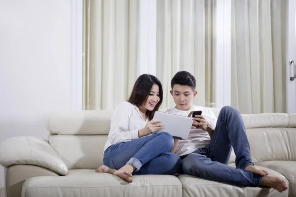 Азиатская пара с планшетом и телефоном дома — стоковое фото
