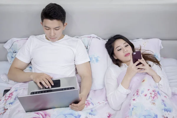 Jeune couple utilisant des appareils numériques avant de dormir — Photo