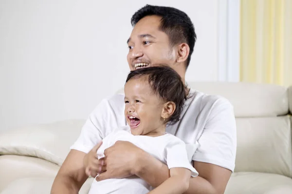 Vreugdevol klein meisje en vader lachen op sofa — Stockfoto