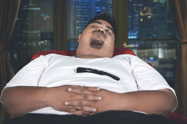 Överviktiga mannen sover med en fjärrkontroll — Stockfoto