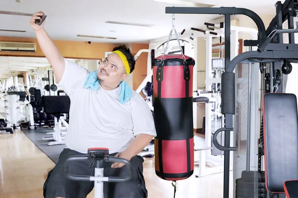 Obese man takes picture on an exercise bike — Stock Photo, Image