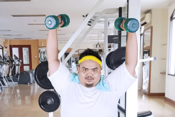 Homem com excesso de peso levanta halteres no centro de fitness — Fotografia de Stock
