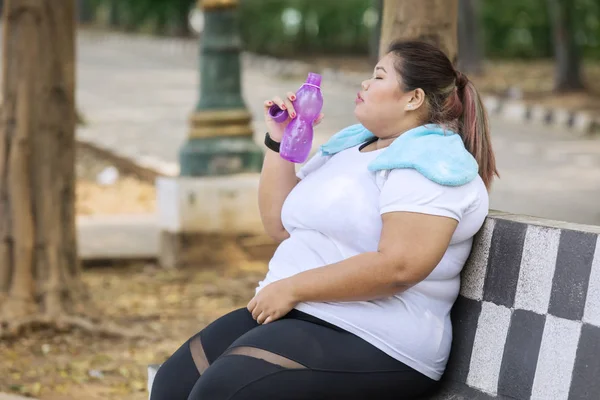 Mulher com excesso de peso bebe água mineral no parque — Fotografia de Stock