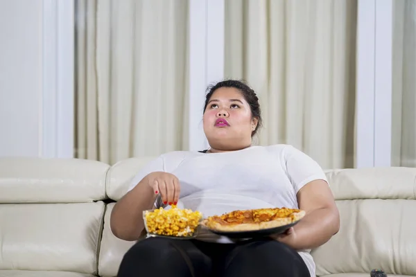 Mulher com excesso de peso comendo lanche enquanto assiste TV — Fotografia de Stock