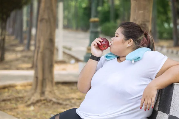 Übergewichtige Frau sitzt im Park und isst Apfel — Stockfoto