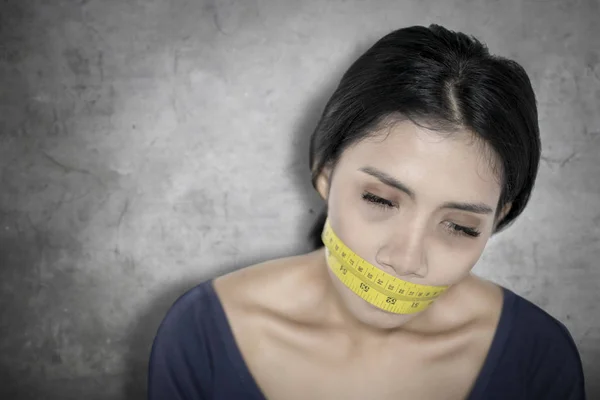 Weary woman covers her mouth with measure tape