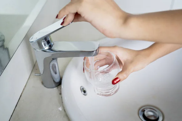 Vrouw de hand giet water uit een kraan in glas — Stockfoto