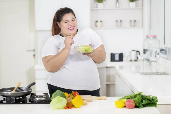 Gülümseyen şişman kadın mutfakta sağlıklı bir salata yiyor — Stok fotoğraf