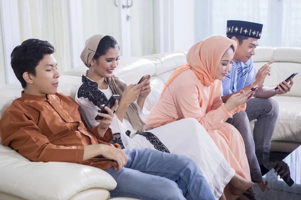 Vier muslimische Menschen, die auf der Couch telefonieren — Stockfoto