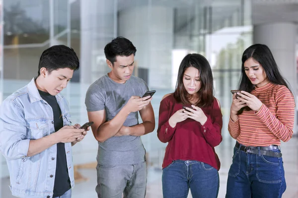Cuatro jóvenes se ven ocupados con los teléfonos móviles —  Fotos de Stock