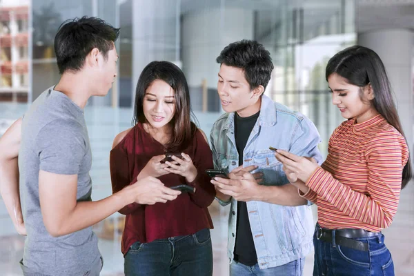 Τέσσερα νεαρά άτομα που χρησιμοποιούν μαζί smartphone — Φωτογραφία Αρχείου