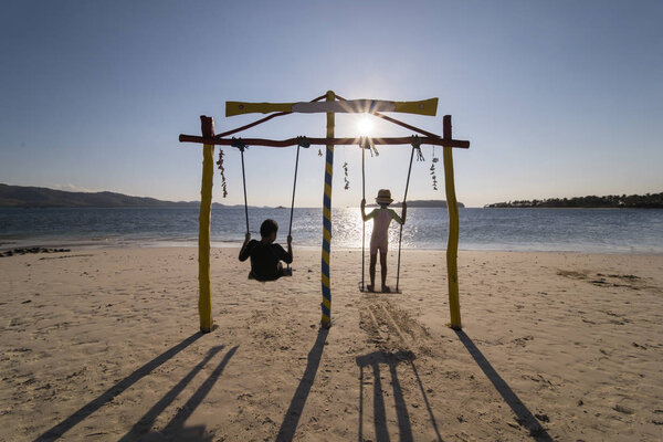 Two little kids enjoy sunset view on a swing